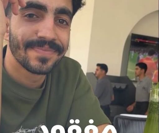 Close-up of a smiling man with a beard in a green shirt at a cafe; Arabic text 'مفقود' across the bottom.