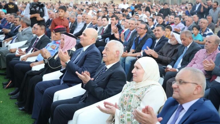 العيسوي 1 - الصافي نيوز Audience of men and women seated outdoors, many clapping, foreground includes a man in a suit and a woman in a hijab